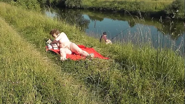 Heta MILF sexy Frina on river bank undressed and sunbathes naked. Random man fisherman watching for her, and in the end decided to join naked woman. Wild beach. Nudist beach. Public nudity. Public exposure. Naked in public klipp Videor